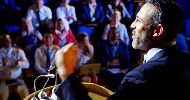 Side view of mature Caucasian businessman speaking in business seminar on stage in auditorium. Audience listening and applauding him 4k 