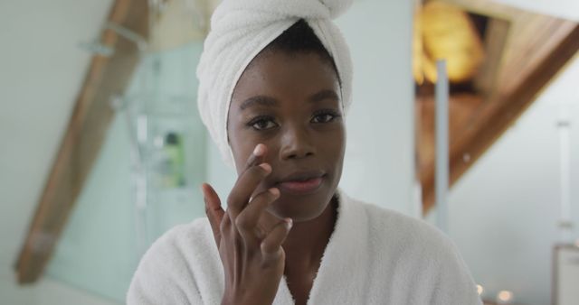 Portrait of african american attractive woman taking care of face and looking at camera in bathroom. beauty, pampering, home spa and wellbeing concept.