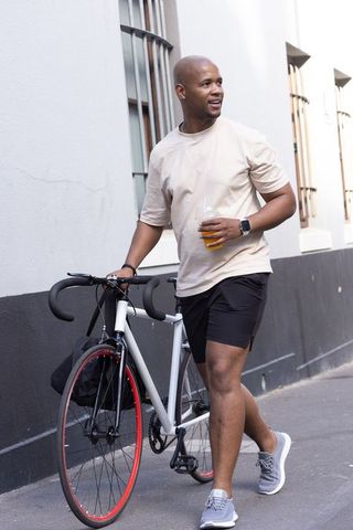 African american man walking with road bike and orange juice on urban sidewalk
