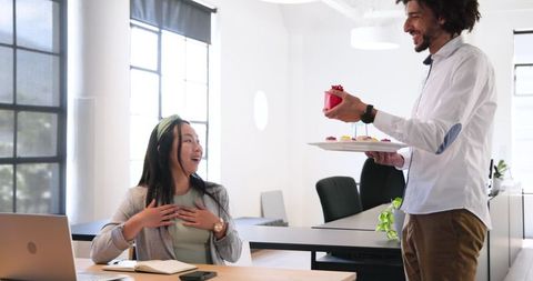 Surprised businesswoman receiving gift from colleague in office