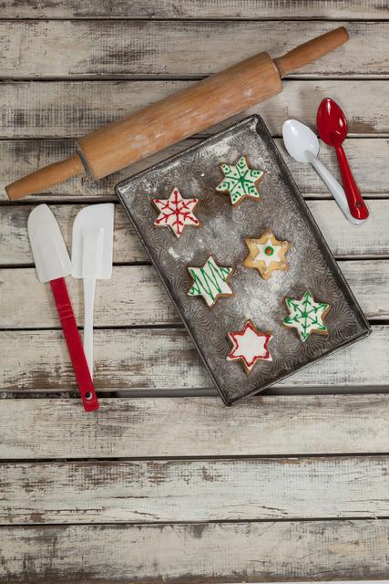 Spatula, spoon, rolling pin and tray with baked Christmas cookies kept on wooden table