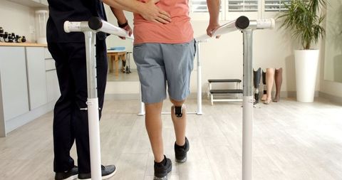 Mature patient walking on prosthetic leg with therapist assistance in clinic