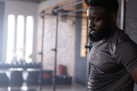 Focused african american athlete resting between sets in industrial gym with squat rack