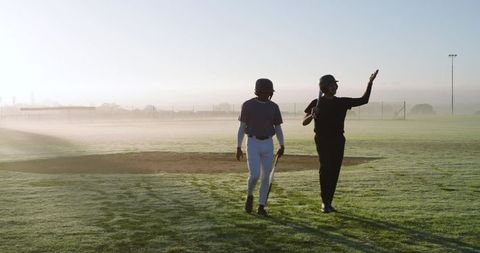 Dawn Mentoring on Dewy Baseball Diamond: Coach Guiding Teen Player with Bat