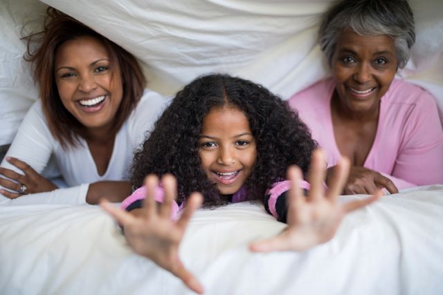 Portrait of happy family lying under blanket on bed in bedroom at home