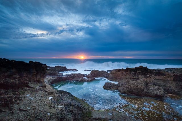 Capturing the stunning sunset over the ocean with dramatic skies and waves hitting the rocky coast creating a serene and tranquil ambiance. Ideal for use in themes related to nature beauty, travel, relaxation, and outdoor activities.