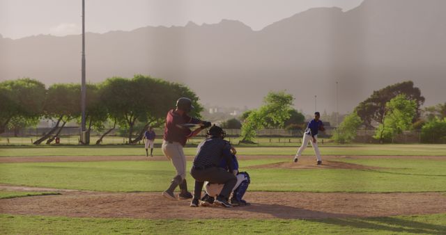 Young baseball players taking part in a game during sunset at a scenic field with mountains in the background. Ideal for sports articles, recreational activity promotions, youth sports programs marketing, and outdoor lifestyle campaigns.