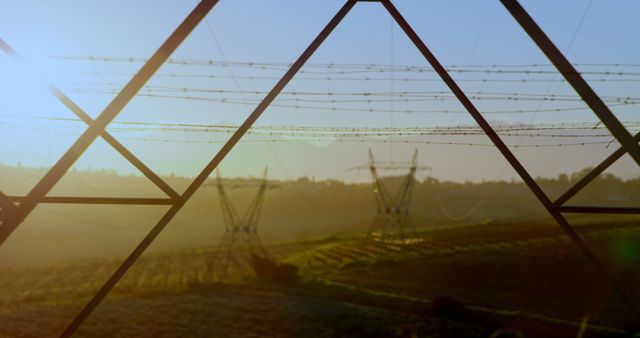 High voltage power lines stretch across rural fields at sunrise, highlighting infrastructure in an agricultural landscape. Suitable for use in content related to energy, environment, rural life, and infrastructure projects.