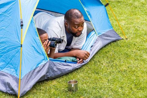 African american father and son camping together in blue tent exploring nature with binoculars