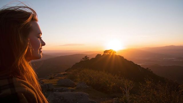 Woman gazing at mountain sunset on rocky ridge with golden sun rays
