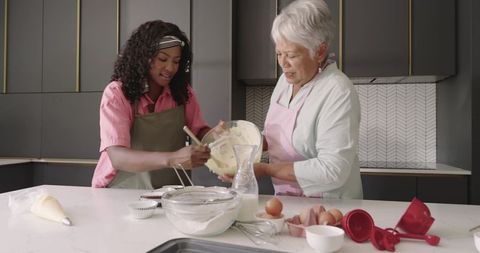 Senior and african american women mixing cake batter in modern kitchen, baking together
