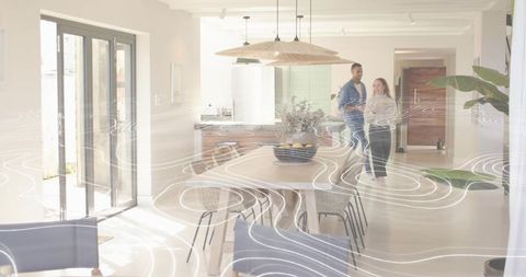 Standing couple chatting in sunlit modern open-plan kitchen with dining table and plants