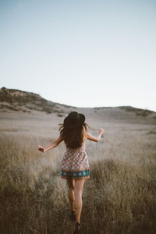 Woman running in field with wide-brimmed hat at dusk