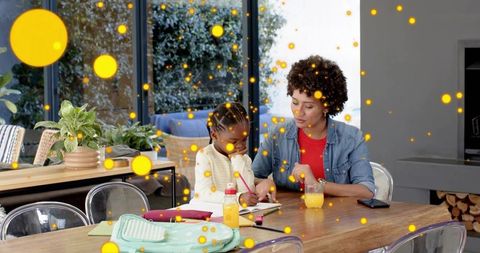 Mother tutoring daughter at dining table helping with homework and writing cozy home