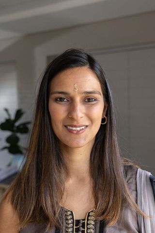 Smiling indian woman wearing embroidered top and bindi, indoor portrait with natural light
