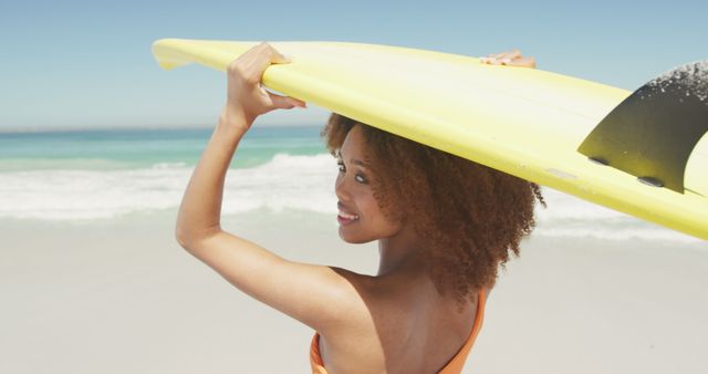 Biracial woman standing on beach, holding surfboard on head and smiling. Summer, vacation, relaxation, happy time.
