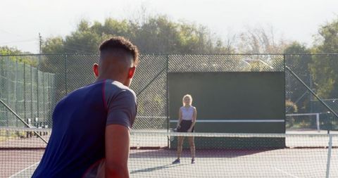 Diverse male and female playing tennis on sunny outdoor court practicing drills and rally