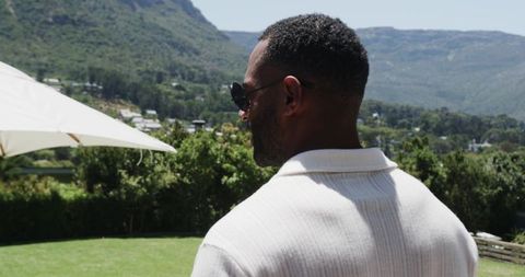 Mature african-american man standing on terrace gazing over lawn and mountain valley view