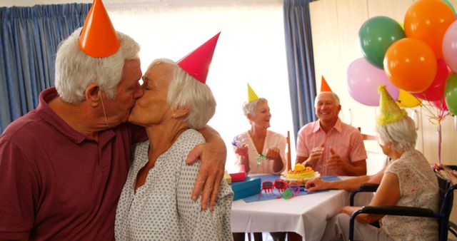 Senior couple kissing and hugging while celebrating birthday with friends at home 