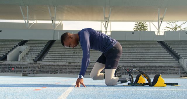 A teenage biracial boy prepares at the starting line on a track field. He's focused on his sprint training at an outdoor sports stadium.