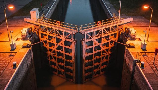 Symmetrical canal lock gates at night with x-braced steel, amber lighting, reflections