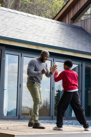 African american father practicing playful sparring with son on modern deck outdoors