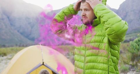 Frustrated camper wearing lime puffer jacket holding head beside yellow tent amid pink smoke