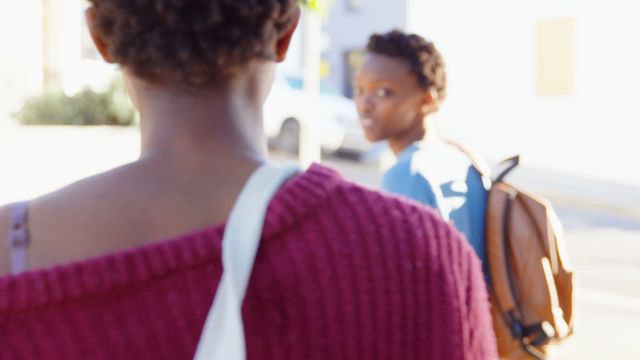 African American twin sisters walking together in a city, with one carrying a bag over her shoulder. They are engaging in conversation, displaying connection and togetherness. Can be used for concepts of sibling relationships, urban lifestyle, casual interactions, and family bonds.