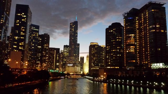 Scenic view of Chicago skyline during dusk with skyscrapers' lights reflecting on the river. Suitable for travel brochures, cityscape collections, evening urban scenes, and articles about Chicago.