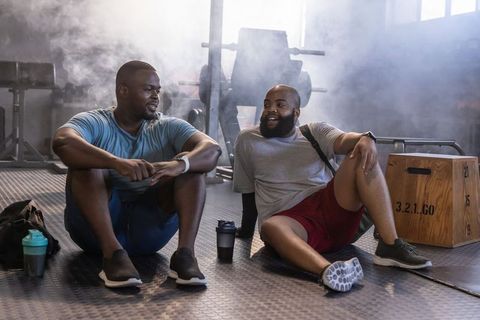 African men resting and laughing after intense workout in industrial gym with equipment