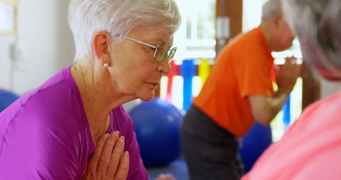 Senior woman practicing yoga with prayer pose in class