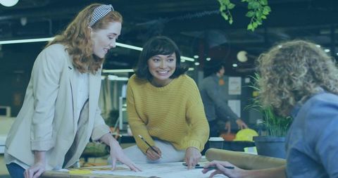 Creative team collaborating over blueprint in modern coworking office with indoor greenery