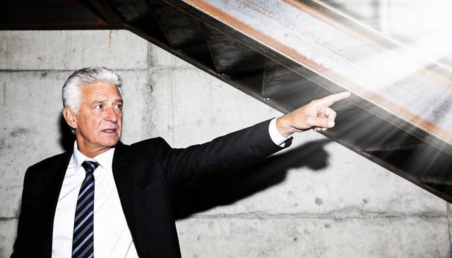 Mature executive pointing upward in industrial stairwell with dramatic spotlight