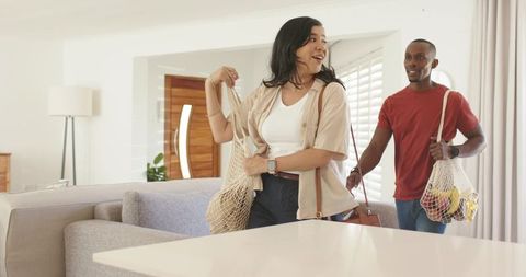 Couple arriving home carrying reusable mesh produce bags in bright modern kitchen