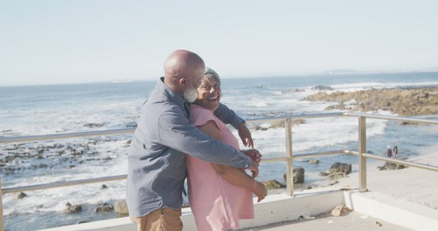 Senior couple embracing on oceanside boardwalk, showing affection and contentment. Ideal for use in ads or brochures related to retirement living, travel services for seniors, health care promotions, or lifestyle blogs emphasizing relationships and enjoying life in later years.