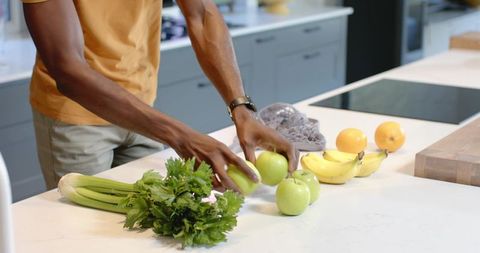 African American man arranging green apples on modern kitchen island with fresh produce