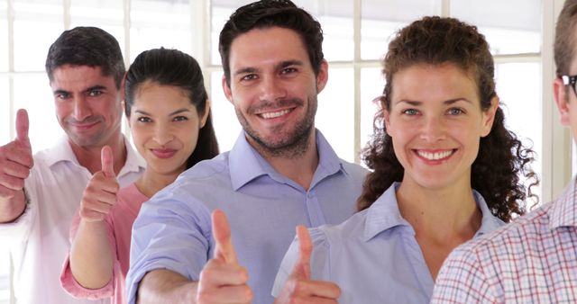 Diverse group of business team members standing in office, smiling and giving thumbs up. Suitable for depicting themes of teamwork, success, collaboration, and positive work environment. Can be used in business promotional materials, corporate websites, and team-building event ads.