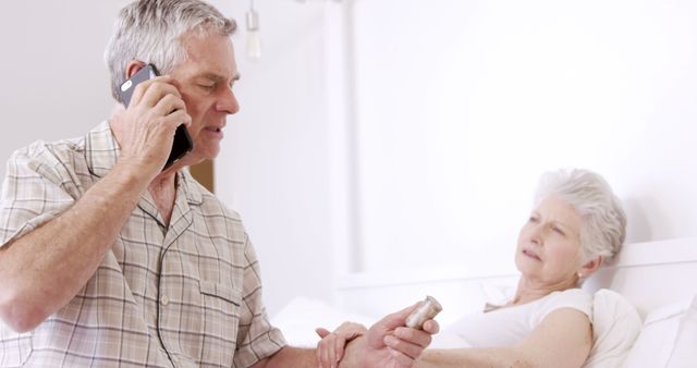 Senior man on phone call holding pills for sick wife in bed