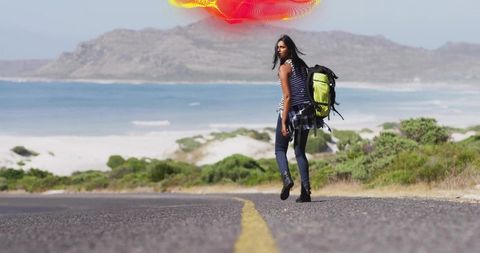 Backpacking woman walking along coastal road looking back with green backpack ocean view