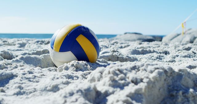 This image features a volleyball resting on a sandy beach with the sea and a clear blue sky in the background. Perfect for promoting beach sports, summer vacation destinations, outdoor recreation, or travel and tourism content. Ideal for use in brochures, travel websites, advertisements for beach gear, and social media campaigns about summer activities.