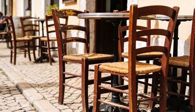 Sunlit rustic bistro chairs with woven seats on european cobblestone sidewalk cafe terrace