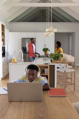 African American family cooking and talking in open-plan kitchen while child studying online