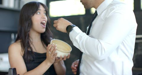 Couple sharing playful feeding moment in kitchen, woman holding bowl while man feeds