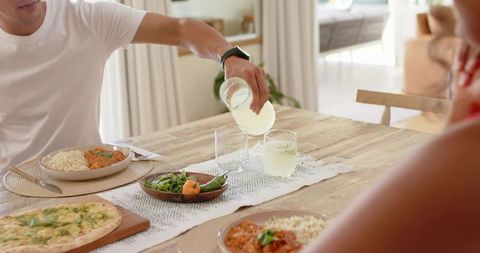 African american couple pouring lemonade at sunlit dining table sharing pizza and salad