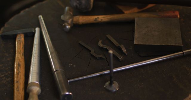 Blacksmithing tools set on a metal workbench, including hammers, tongs, and other metalworking implements. Ideal for illustrating traditional craftsmanship, metal forging processes, and artisan workshops. Suitable for use in articles, presentations, or websites focused on metalworking, blacksmithing, or artisan crafts.