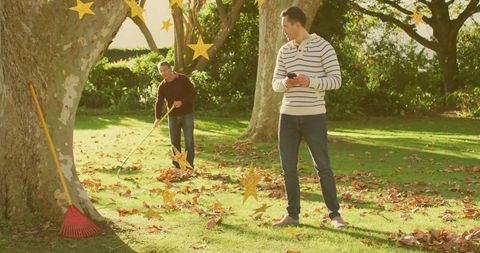 Checking phone while friend raking leaves in sunlit autumn garden with gold star overlays