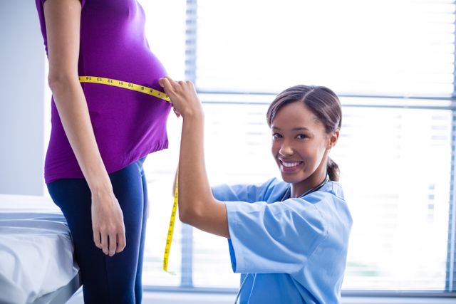 Doctor measuring pregnant woman's belly in hospital. Ideal for use in healthcare, maternity care, prenatal checkup, and pregnancy-related content. Useful for illustrating medical examinations, prenatal care, and expectant mothers receiving healthcare services.