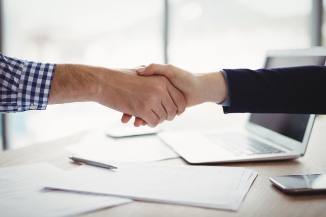 Close-up of executives shaking hands at desk in office