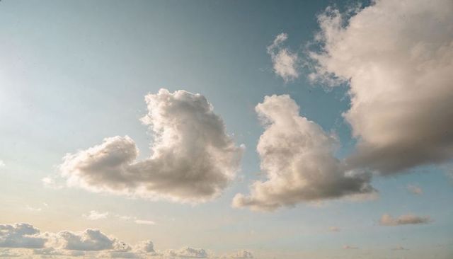 Two Cumulus Clouds Drifting Over Wide Horizon at Golden Hour with Soft Light
