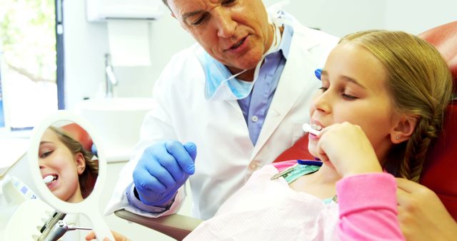 A middle-aged Caucasian dentist is examining a young girl's teeth, with copy space. His professional demeanor and her relaxed posture suggest a comfortable and trusting patient-dentist relationship.